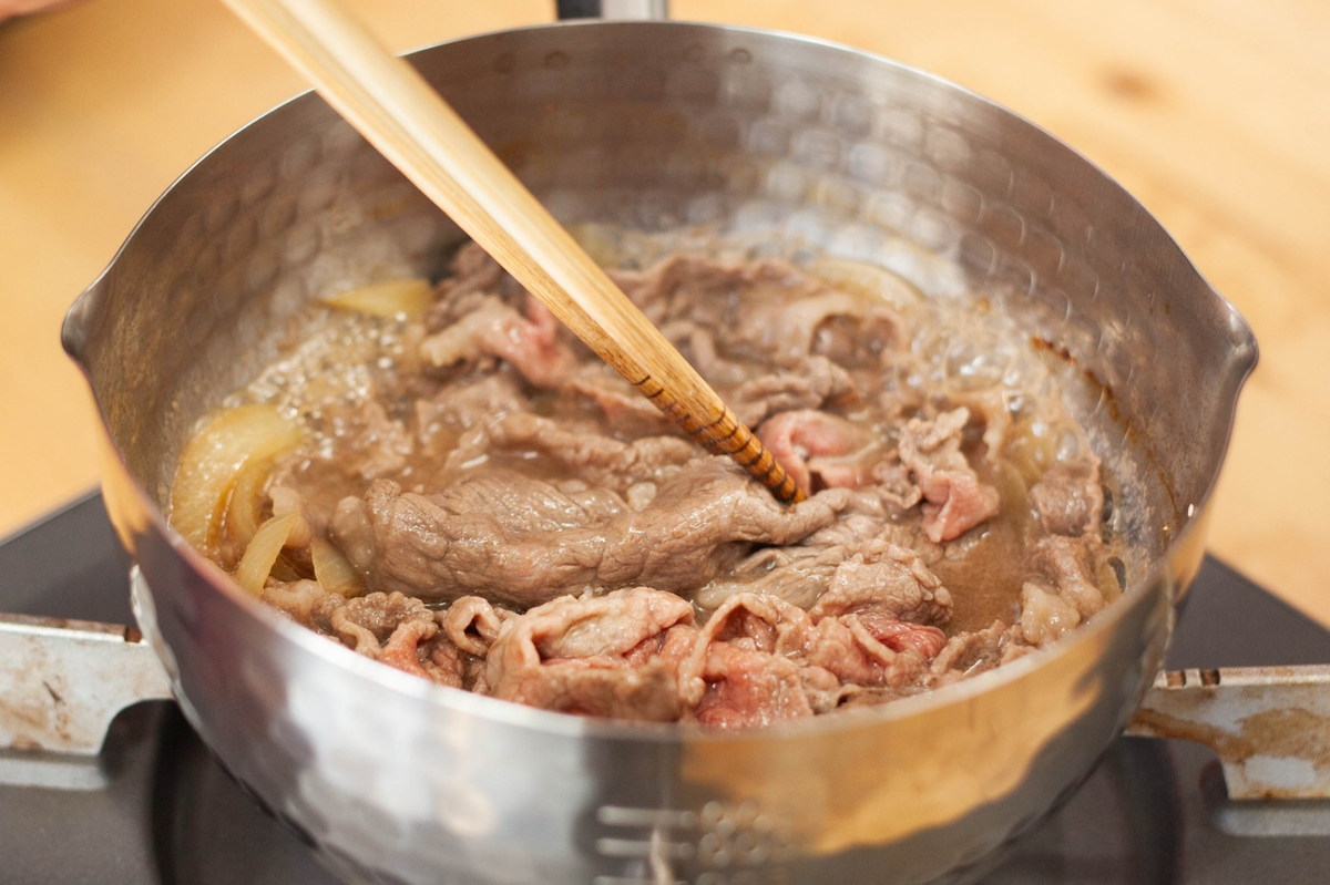 Someone simmering beef with chopsticks in a Yukihira Nabe on a stovetop