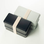 Gel-Cool Two-Tier Bento Box 1000ml in black and light grey, both closed with beige elastic band, shown overlapping at an angle on white background