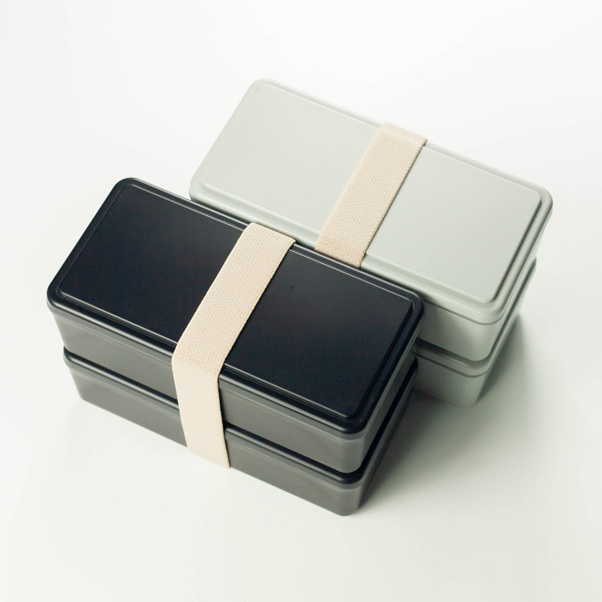 Gel-Cool Two-Tier Bento Box 1000ml in black and light grey, both closed with beige elastic band, shown overlapping at an angle on white background