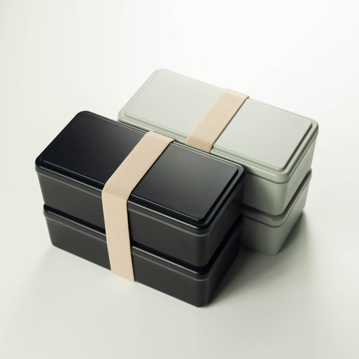 Gel-Cool Two-Tier Bento Box 1000ml in black and light grey, both closed with beige elastic band, shown overlapping from a slightly different angle on white background