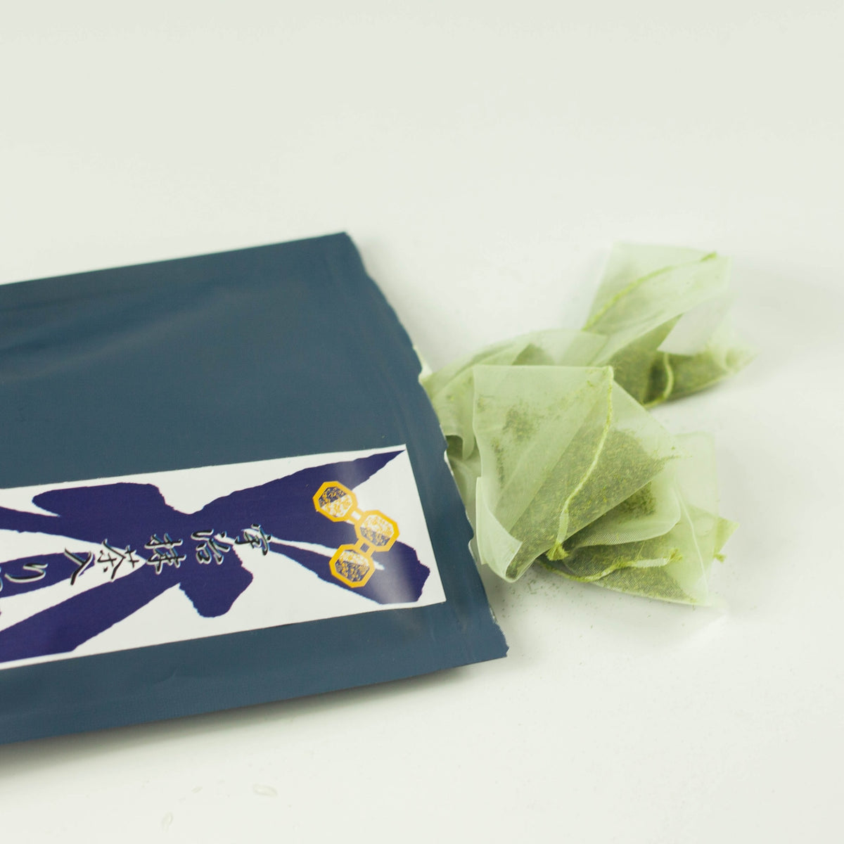 Chikiriya Cold Brew Matcha Green Tea pouch lying flat with two pyramid-shaped green tea bags beside it, showing the tea bag texture and contents, on white background
