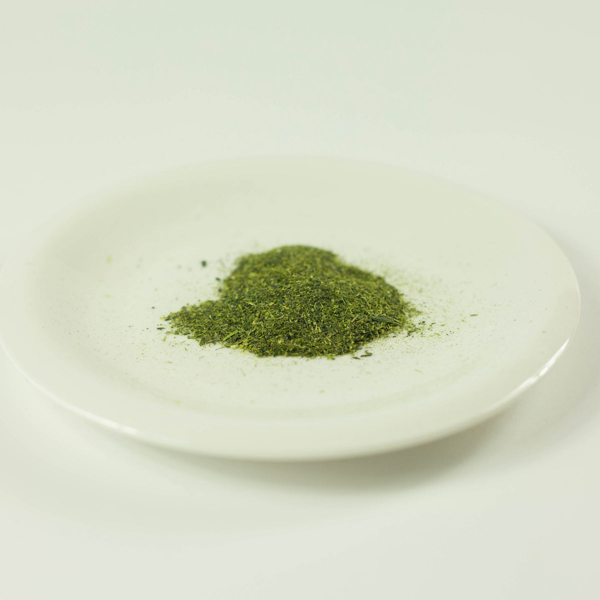 Close-up of loose green tea and matcha powder blend from Chikiriya Cold Brew Matcha Green Tea, piled on a white ceramic plate on white background