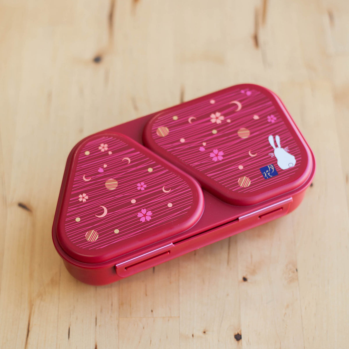 Onigiri Maker Bento Box Moon Rabbit closed, deep red with moon, cherry blossom and white rabbit design on lid, angled view on wooden surface