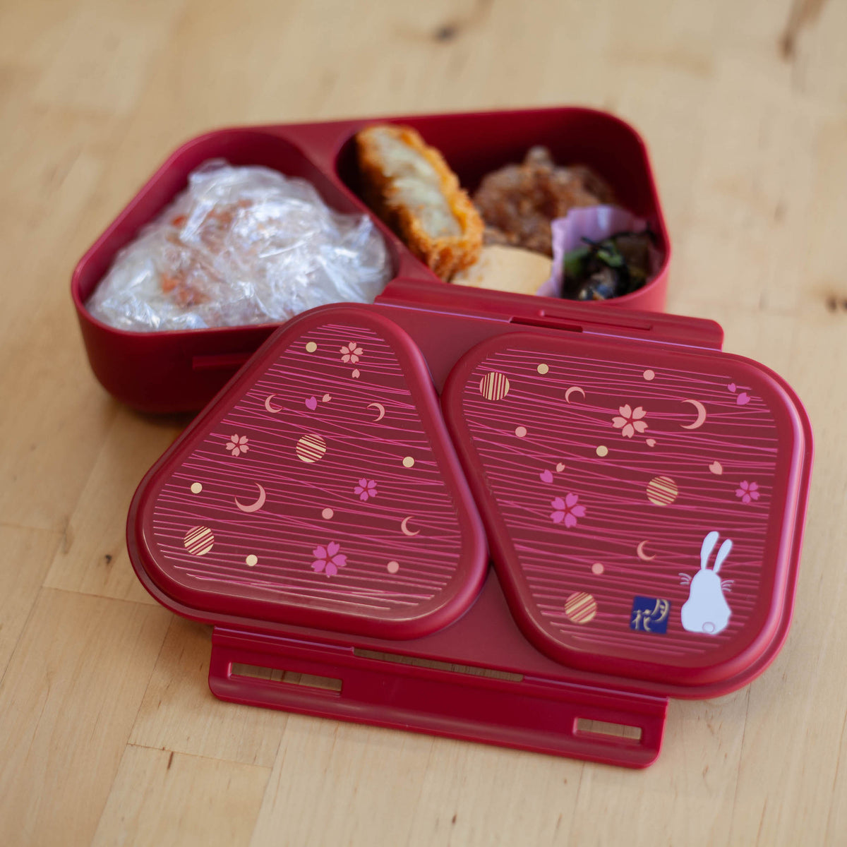 Onigiri Maker Bento Box Moon Rabbit closed, deep red with moon, cherry blossom and white rabbit design on lid, angled view on wooden surface