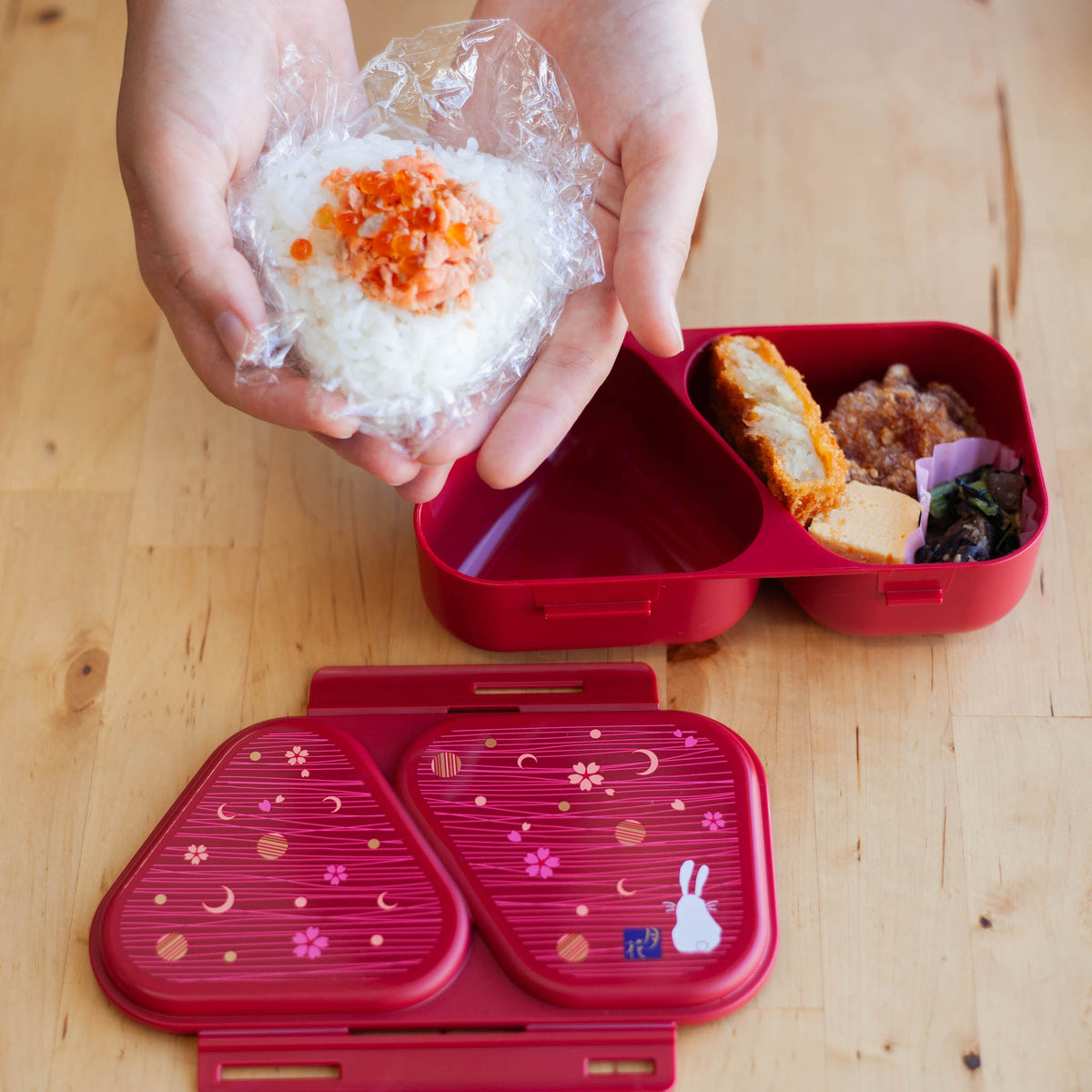 Onigiri Maker Bento Box Moon Rabbit closed, deep red with moon, cherry blossom and white rabbit design on lid, angled view on wooden surface