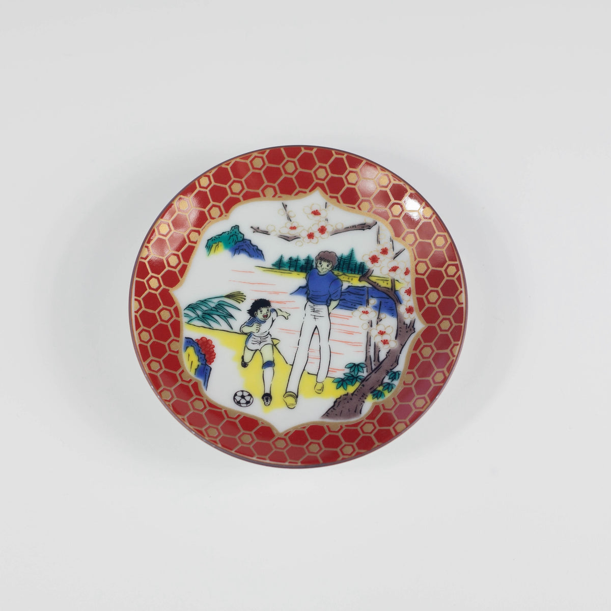 Decorative plate with a red border and colorful design of two people playing soccer on a white background
