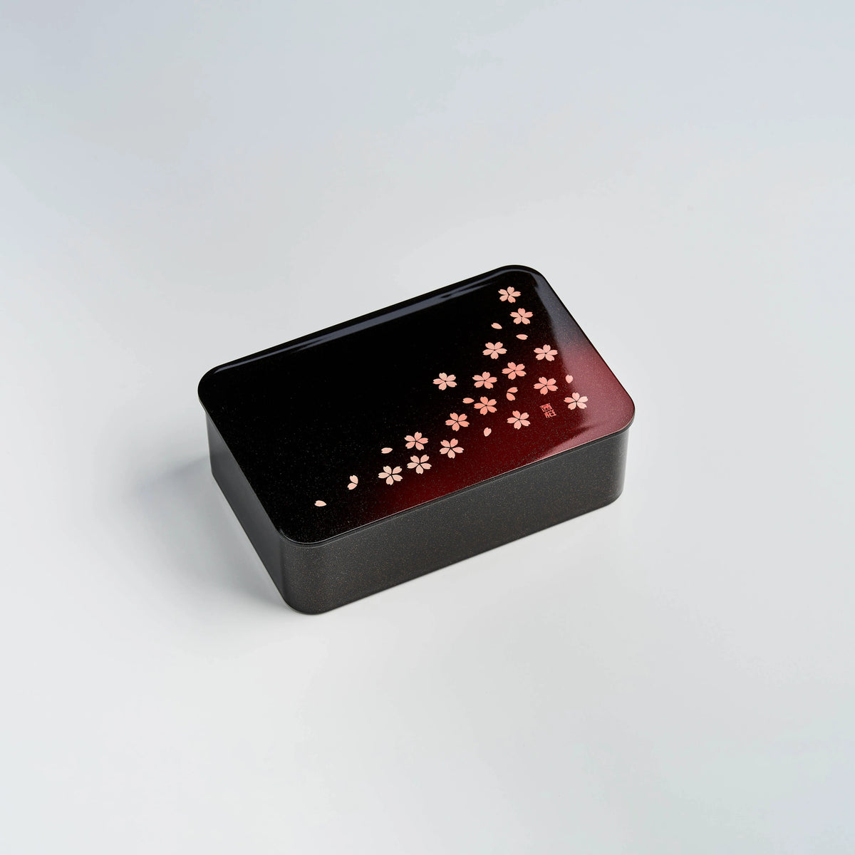 Hakoya Sakura Petals Bento Box closed, black to burgundy gradient lacquer lid with scattered pink cherry blossom pattern, angled view on grey background