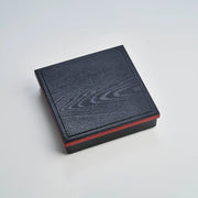 Japanese lacquerware-style bento box with black wood-grain textured lid and dark red base, elegant square lunch box, made in Japan