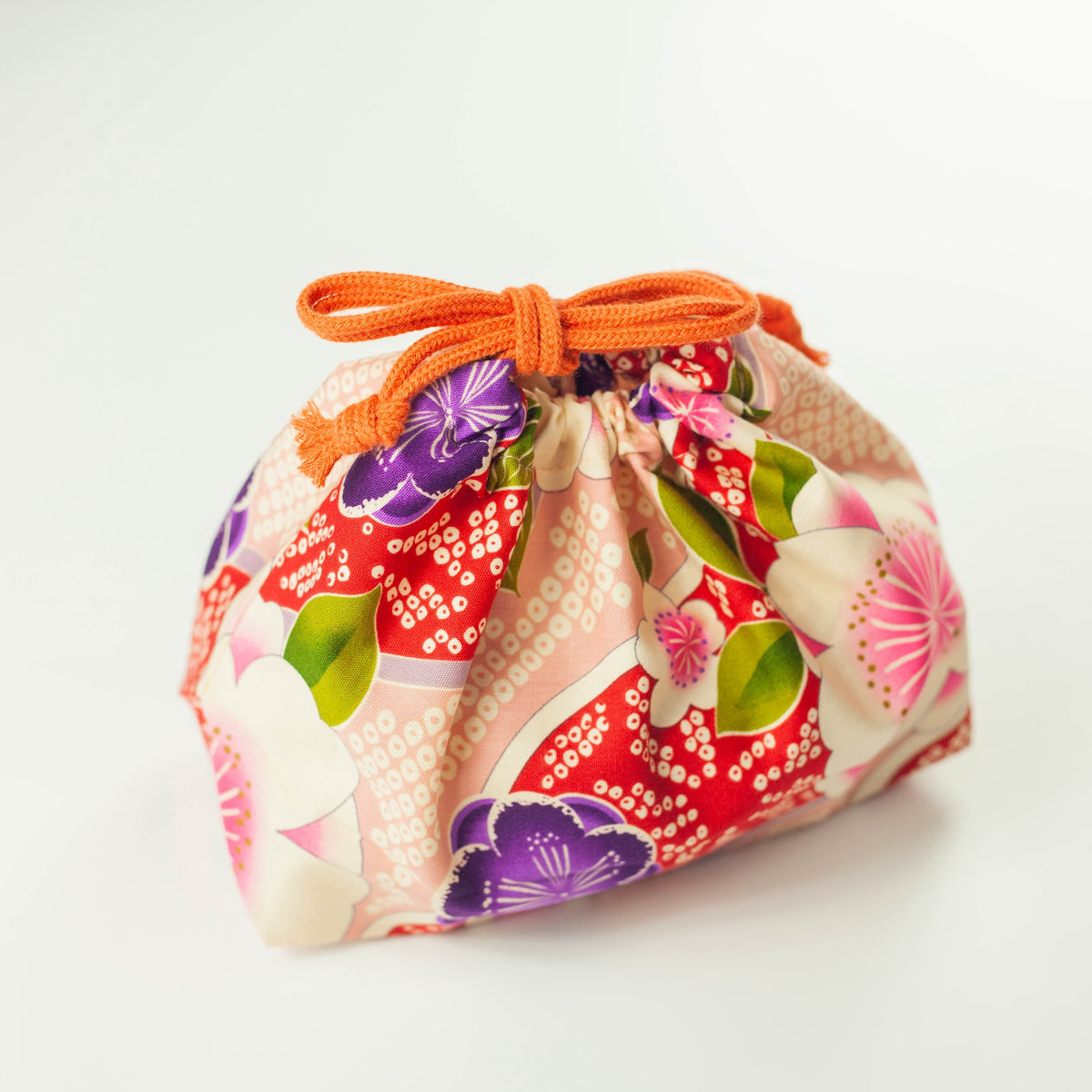 Kimono Sakura Pink bento drawstring bag closed with orange cord tie, pink and red Japanese floral fabric with white sakura, purple and pink flowers, white background