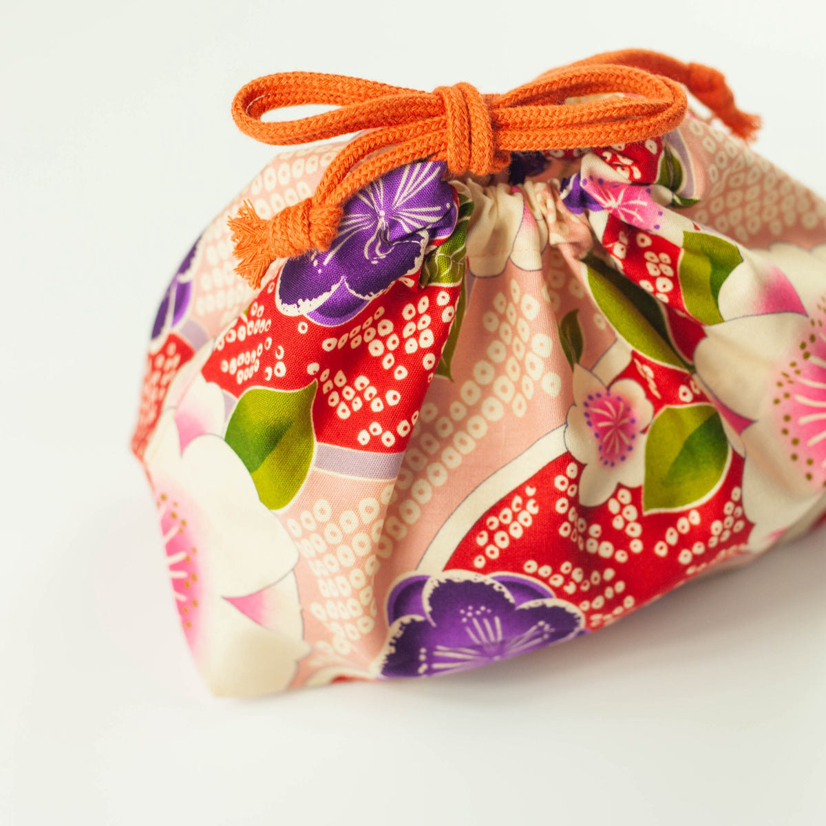 Kimono Sakura Pink bento drawstring bag closed with orange cord tie, pink and red Japanese floral fabric with white sakura, purple and pink flowers, white background