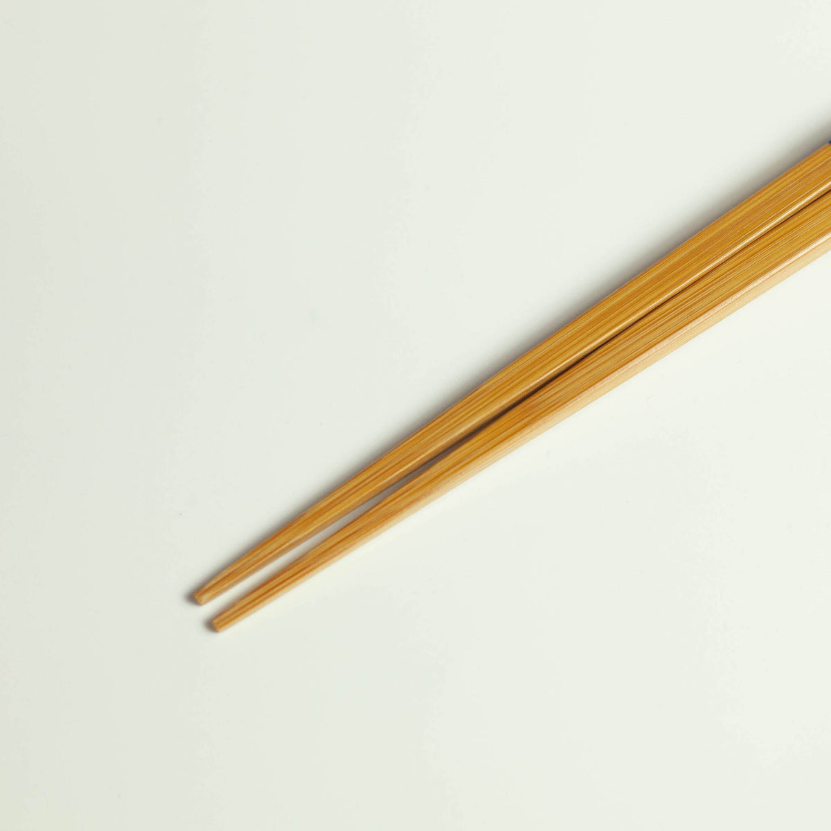 Twisted bamboo chopsticks with blue band, full length diagonal view on white background