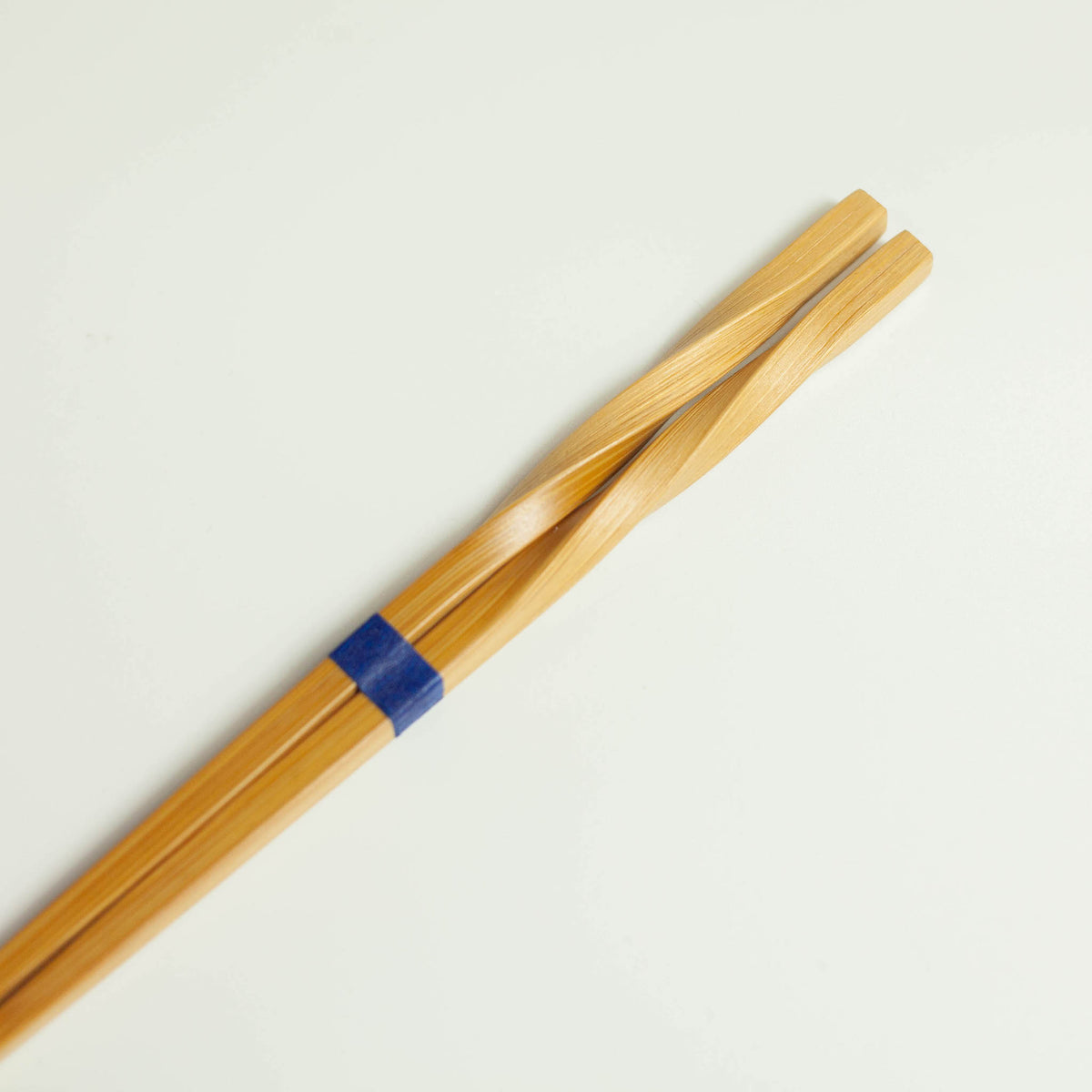 Twisted bamboo chopsticks with blue band, full length diagonal view on white background