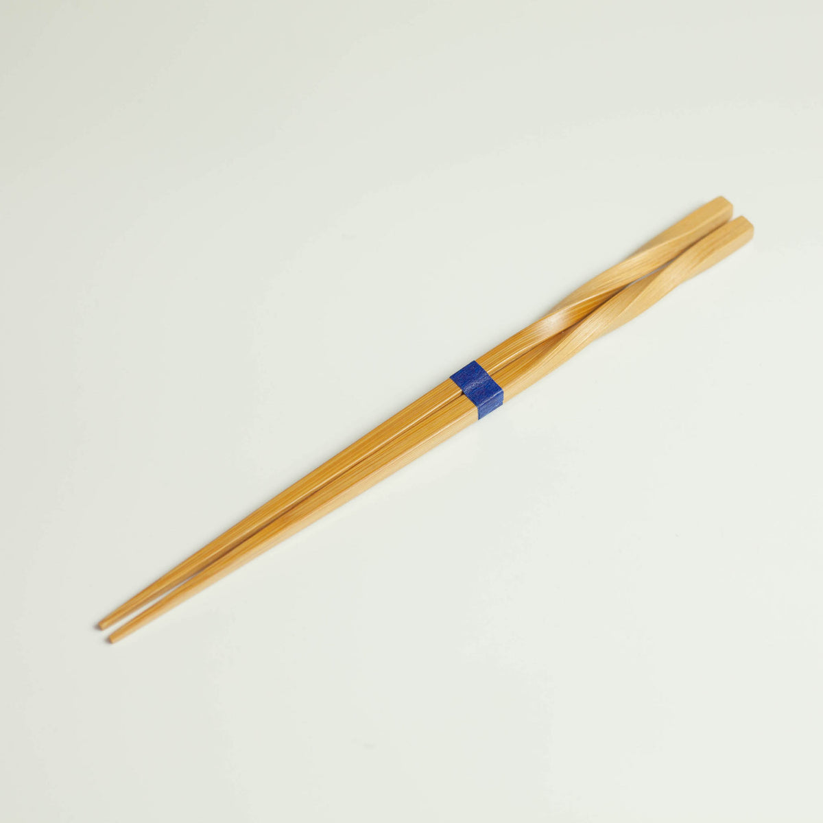 Twisted bamboo chopsticks with blue band, full length diagonal view on white background