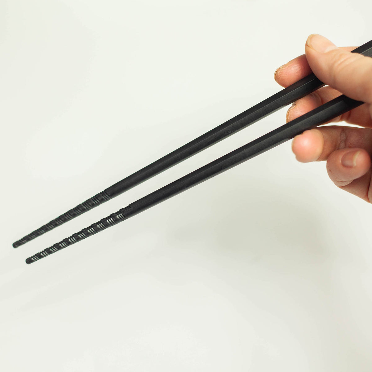Hand holding Tornado Chopsticks – matte black finish with spiral-textured non-slip tips, white background
