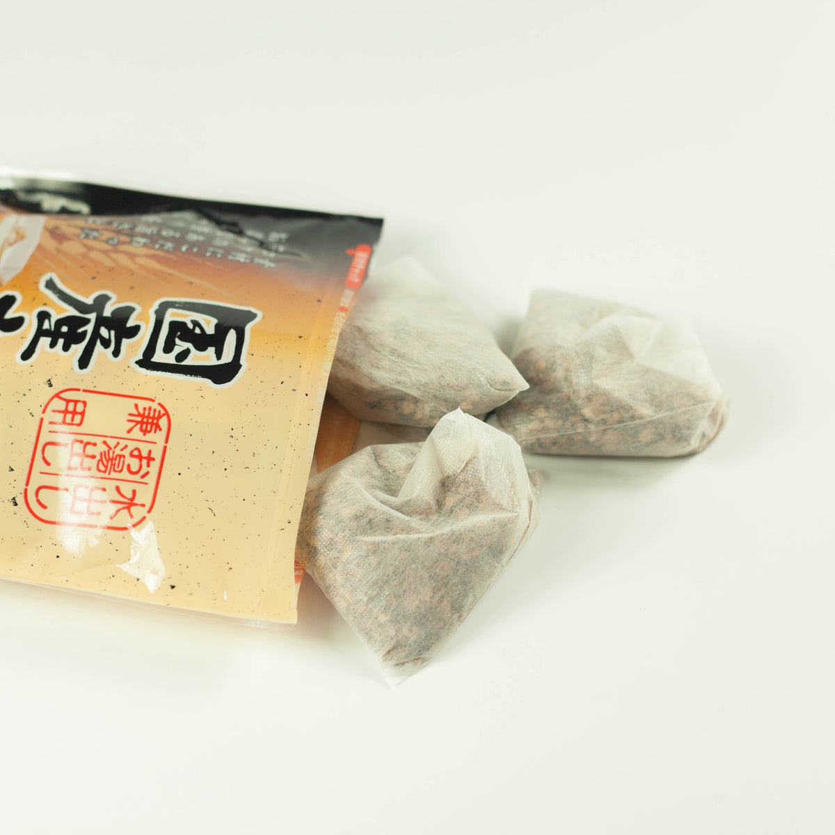 Cold Brew Mugicha Barley Tea pouch lying on its side with three pyramid-shaped tea bags spilling out, on white background