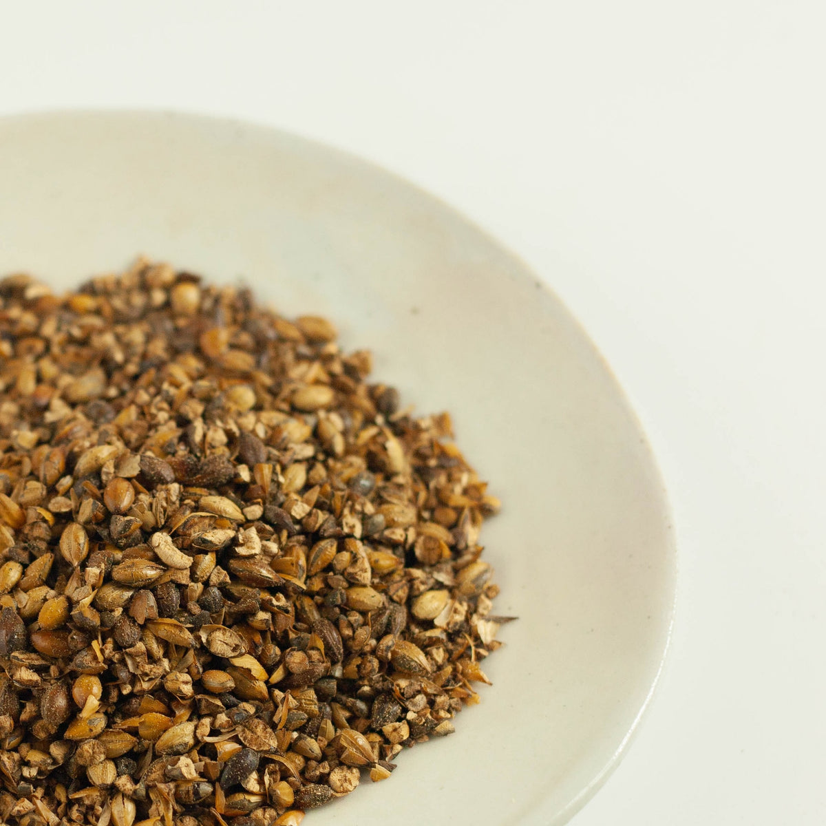 Close-up overhead view of roasted barley grains for mugicha tea piled on a white ceramic plate on white background