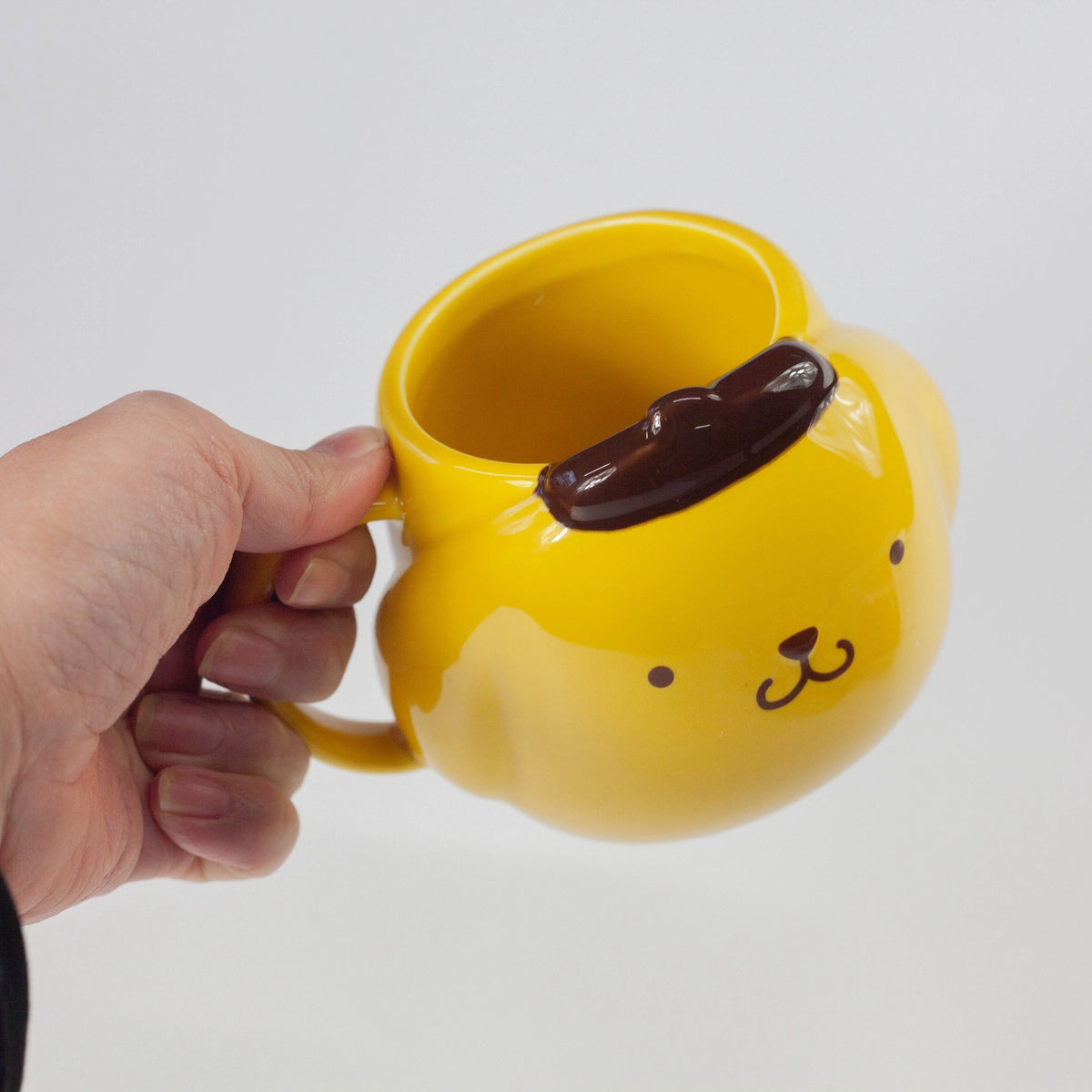 Yellow mug shaped like a dog with a handle, held by a hand against a white background.