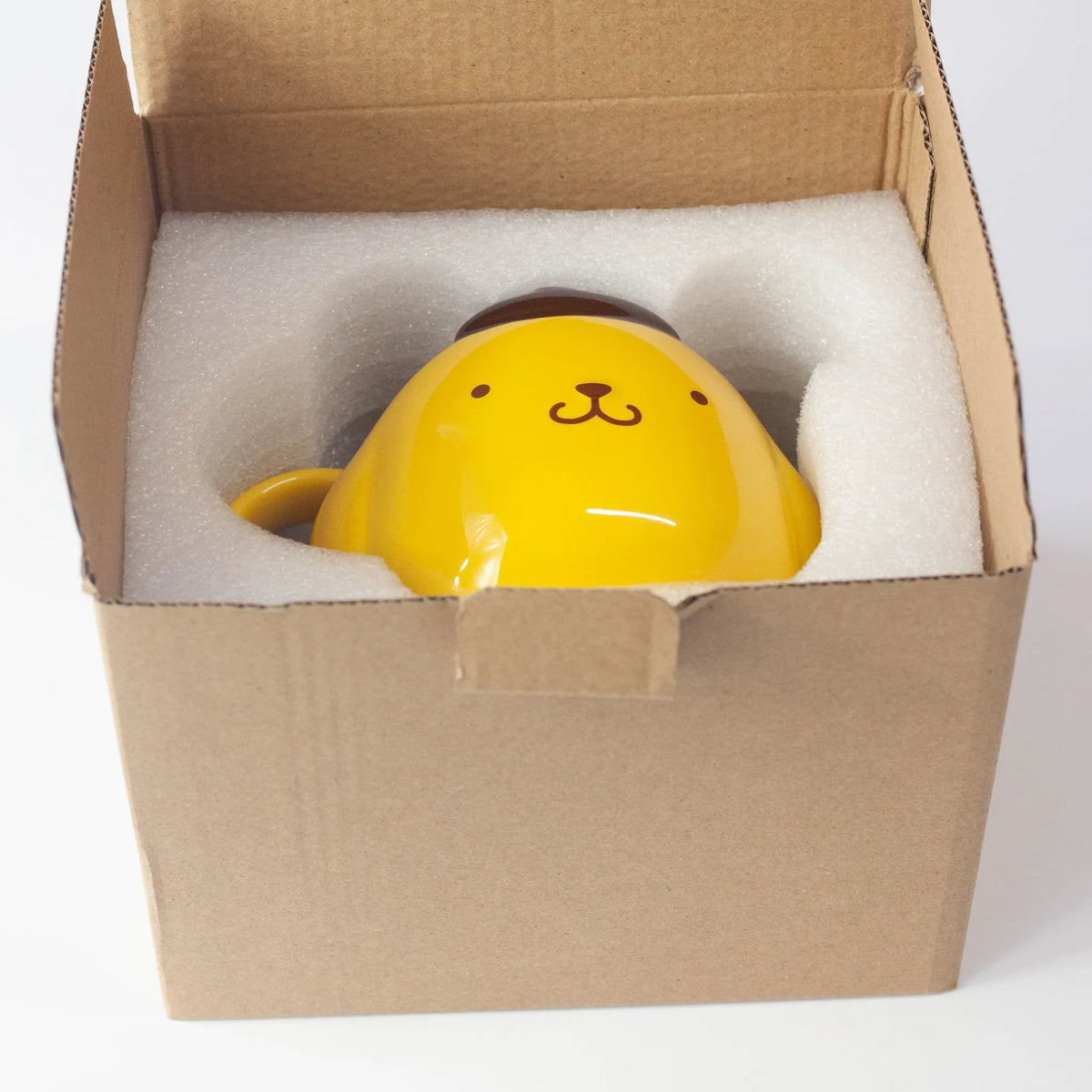 Yellow ceramic mug with a dog face in a cardboard box with foam on a white background