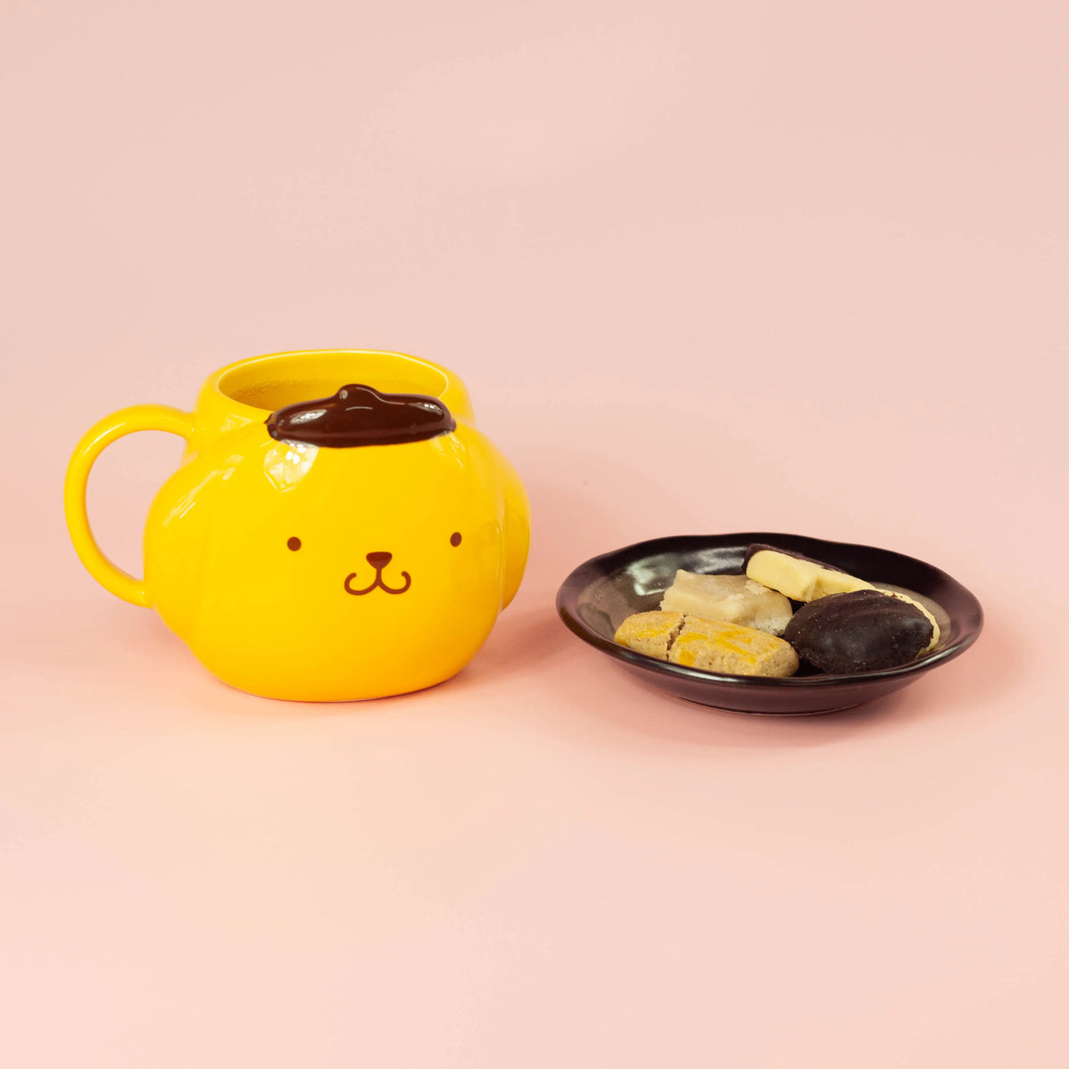Yellow dog-faced mug next to a black plate of cookies on a pink background