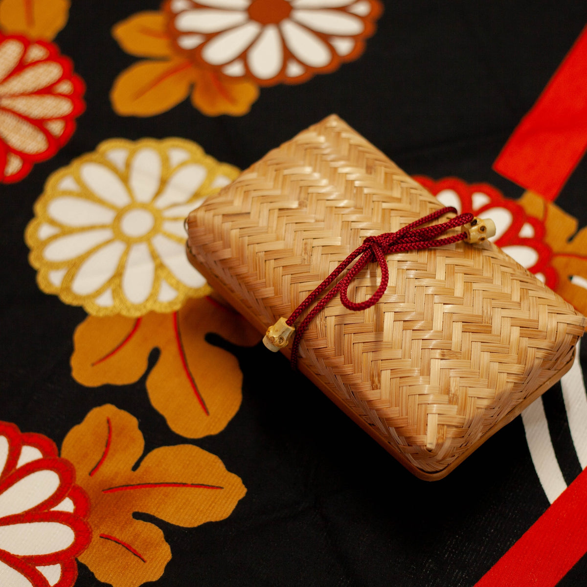 Woven Bamboo Bento Box with red braided cord displayed on black floral furoshiki wrapping cloth