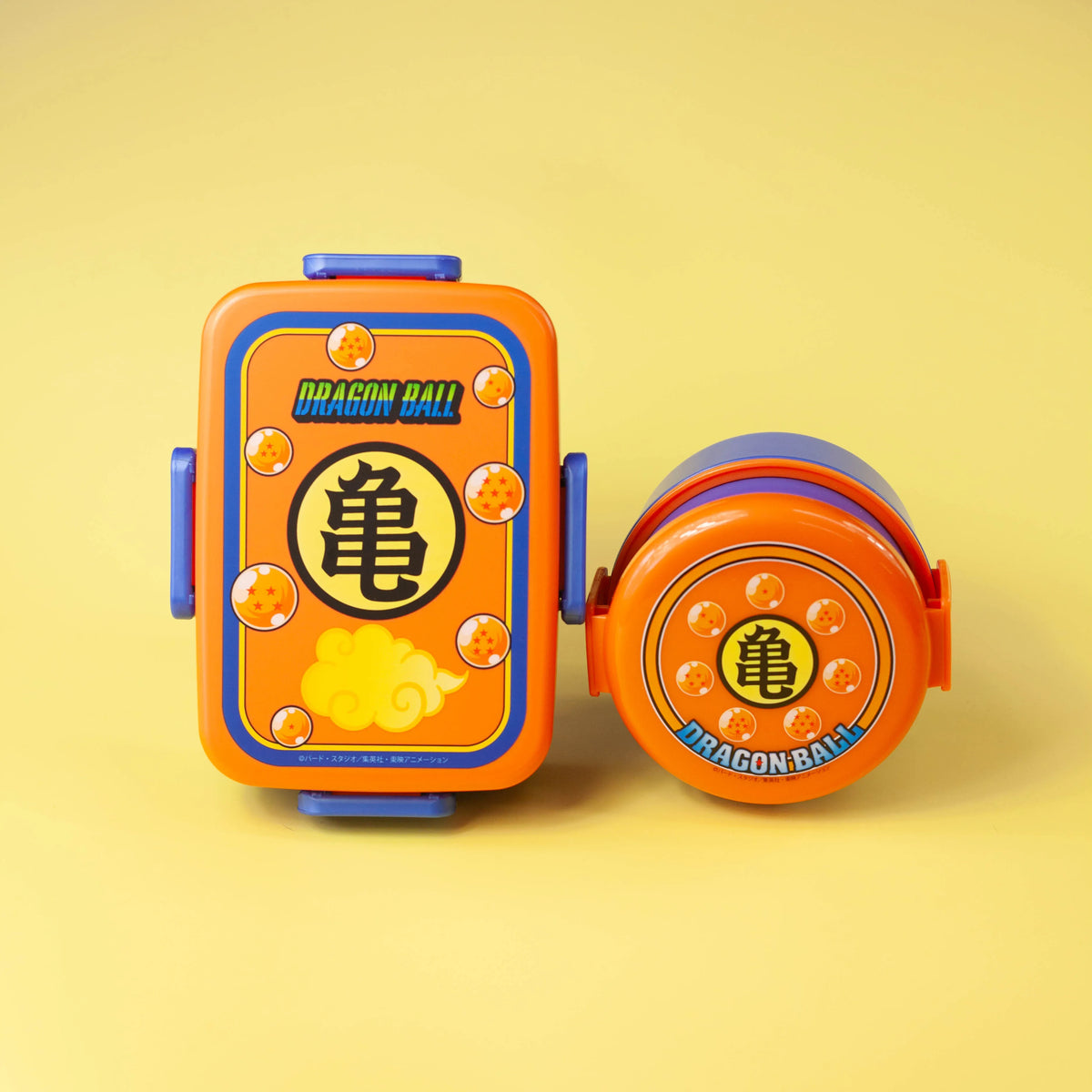 Dragon Ball rectangular and round bento boxes displayed upright on a yellow background with their lid designs facing forward