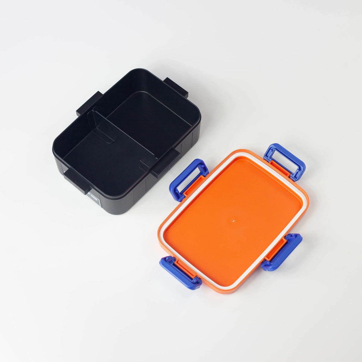Open Dragon Ball bento box showing a black interior with a divider and an orange lid with a white seal and four blue clips