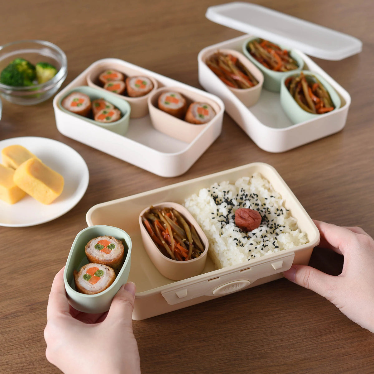 Marumi Silicone Cup Set in use as bento box – hands holding silicone cup with rolled sushi, tray filled with rice and side dishes