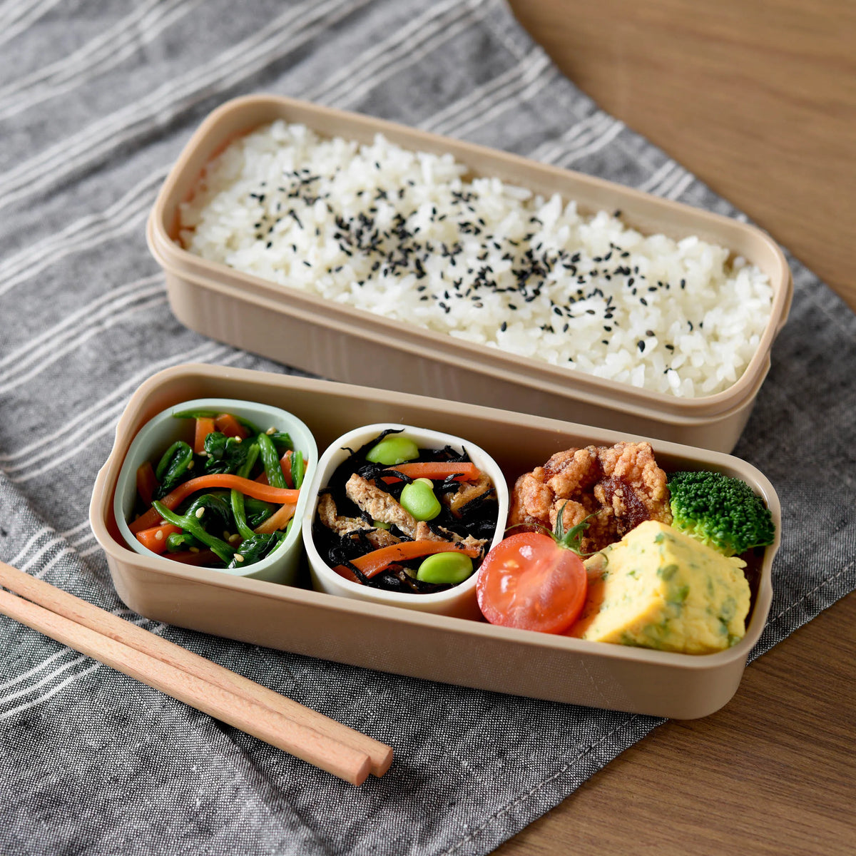 Marumi Silicone Cup Set Round used as two-tier bento box – upper tier with sesame rice, lower tier with spinach stir-fry, hijiki, karaage, broccoli, and tamagoyaki, with wooden chopsticks