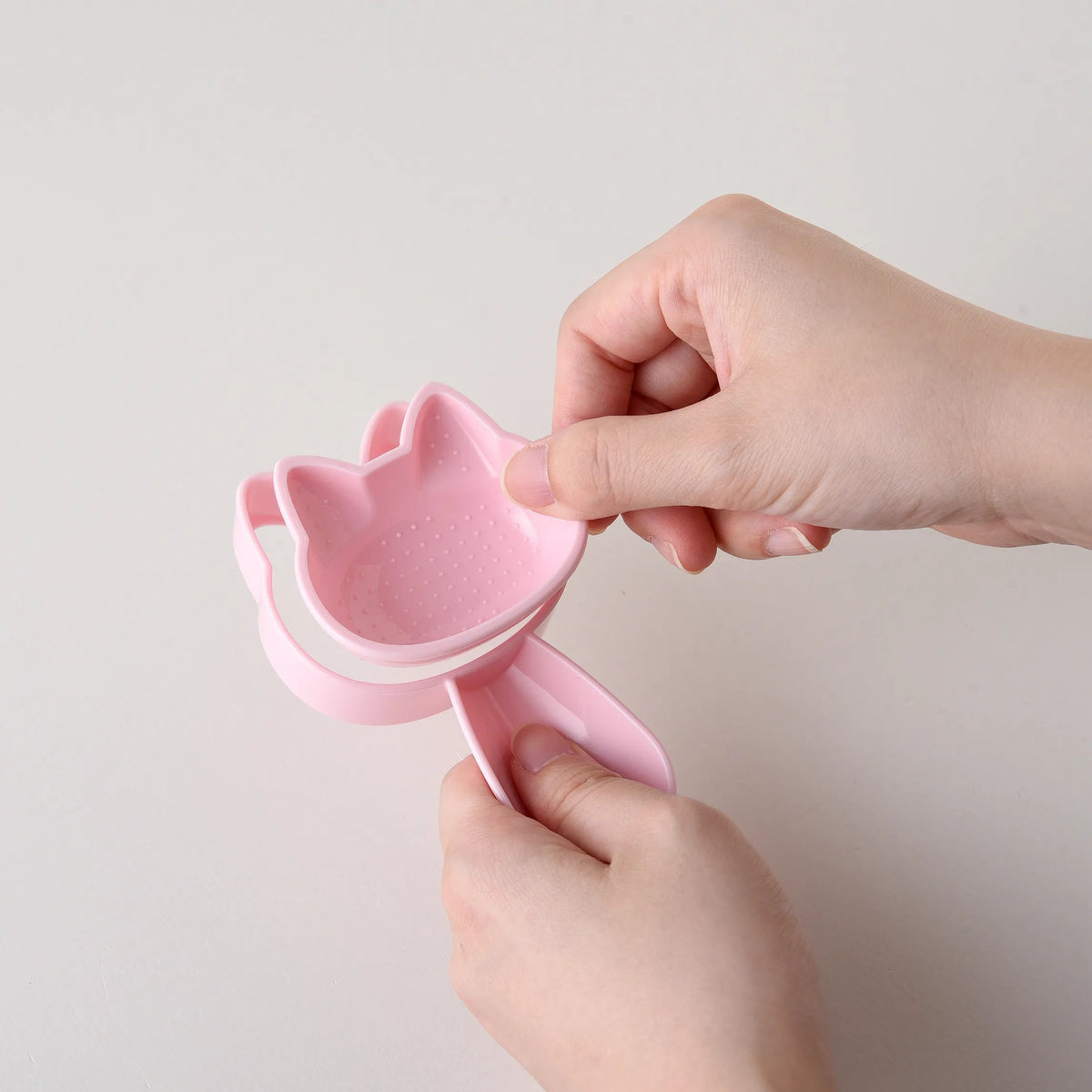 Hands pressing closed the pink cat-shaped onigiri mold from Neko Kao Onigiri Set – compact cat silhouette shape, white background