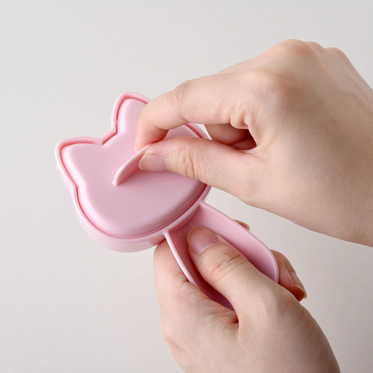 Hands pressing closed the pink cat-shaped onigiri mold from Neko Kao Onigiri Set – compact cat silhouette shape, white background