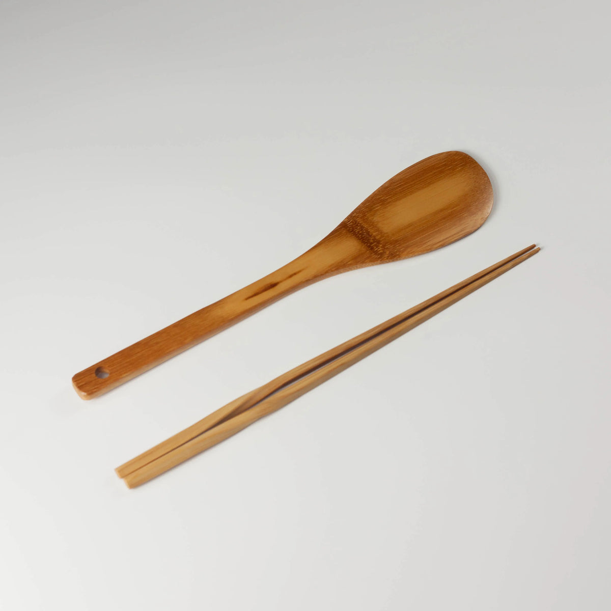 Bamboo kitchen utensils set with a broad cooking spatula and a pair of long chopsticks on a white background