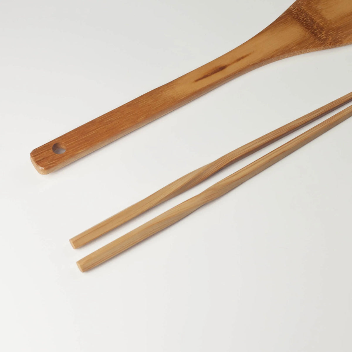 Close-up of the bamboo spatula handle with a hanging hole beside the twisted chopstick handles