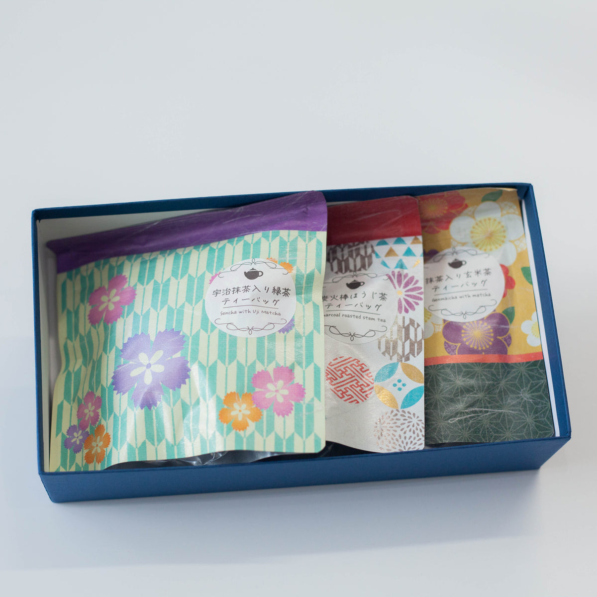 Wafu Japanese Green Tea Gift Set – open dark brown gift box with three colorful floral tea pouches inside: yellow floral sencha, white geometric hojicha, and green floral matcha green tea, on white background