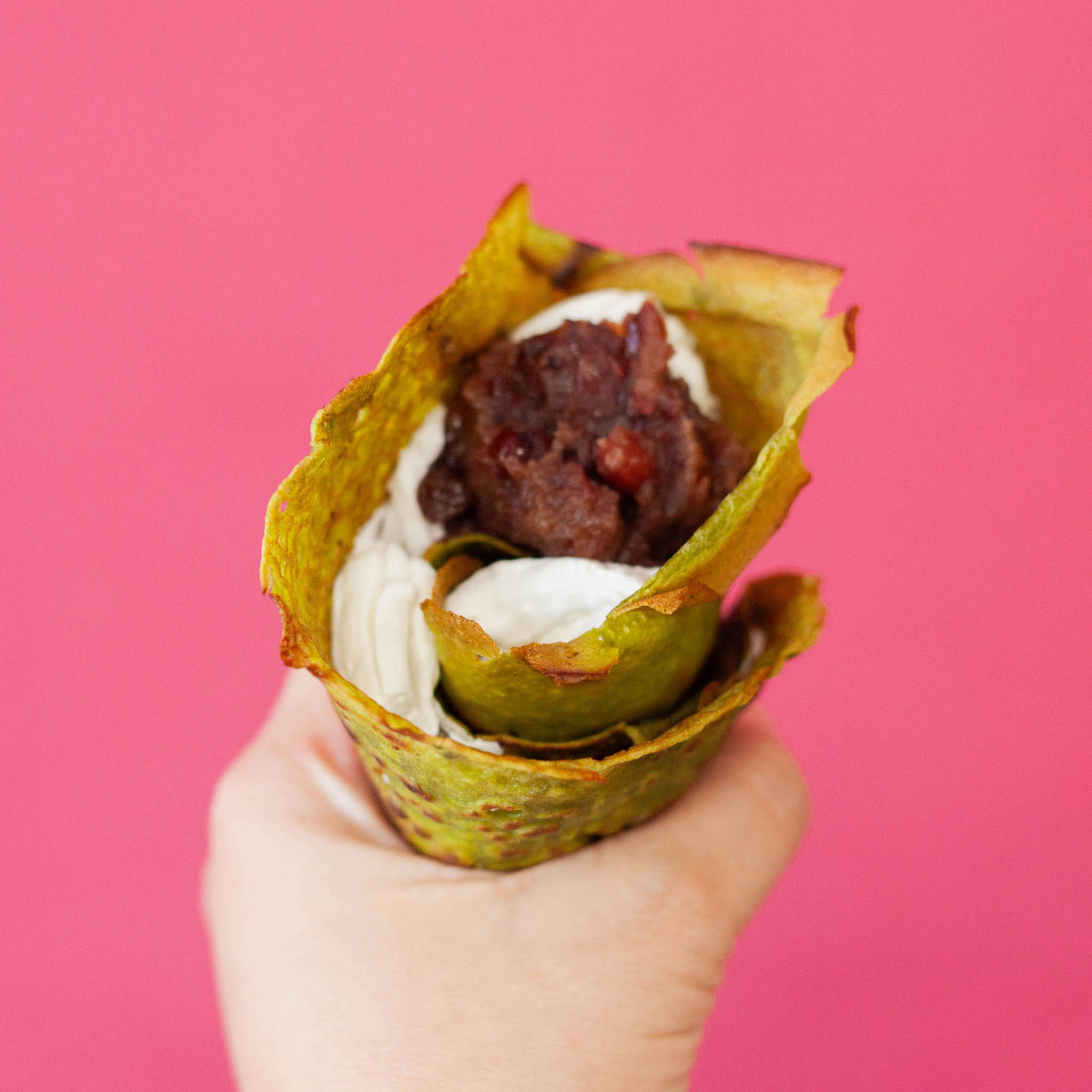 Hand holding a matcha crepe cone filled with whipped cream and red bean paste, made with Chikiriya Shizuoka Matcha Powder, against a bright pink background