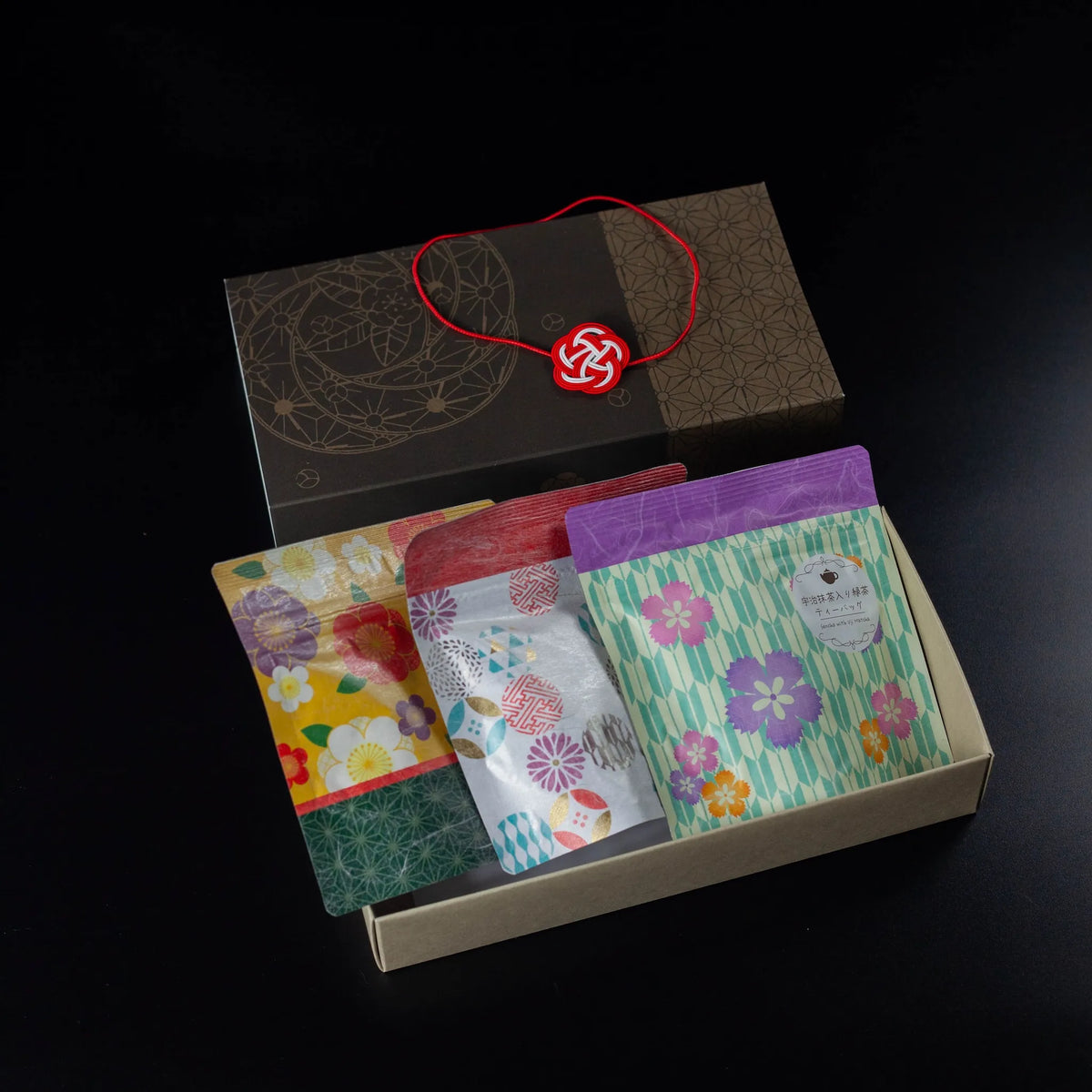 Wafu Japanese Green Tea Gift Set – open dark brown gift box with three colorful floral tea pouches and a red mizuhiki knot decoration beside it, on white background