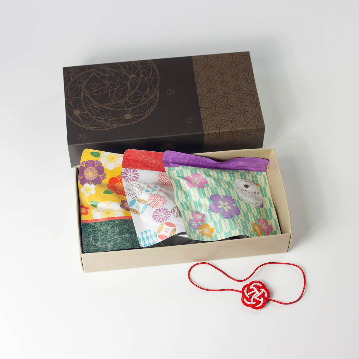 Wafu Japanese Green Tea Gift Set – open dark brown gift box with three colorful floral tea pouches and a red mizuhiki knot decoration beside it, on white background