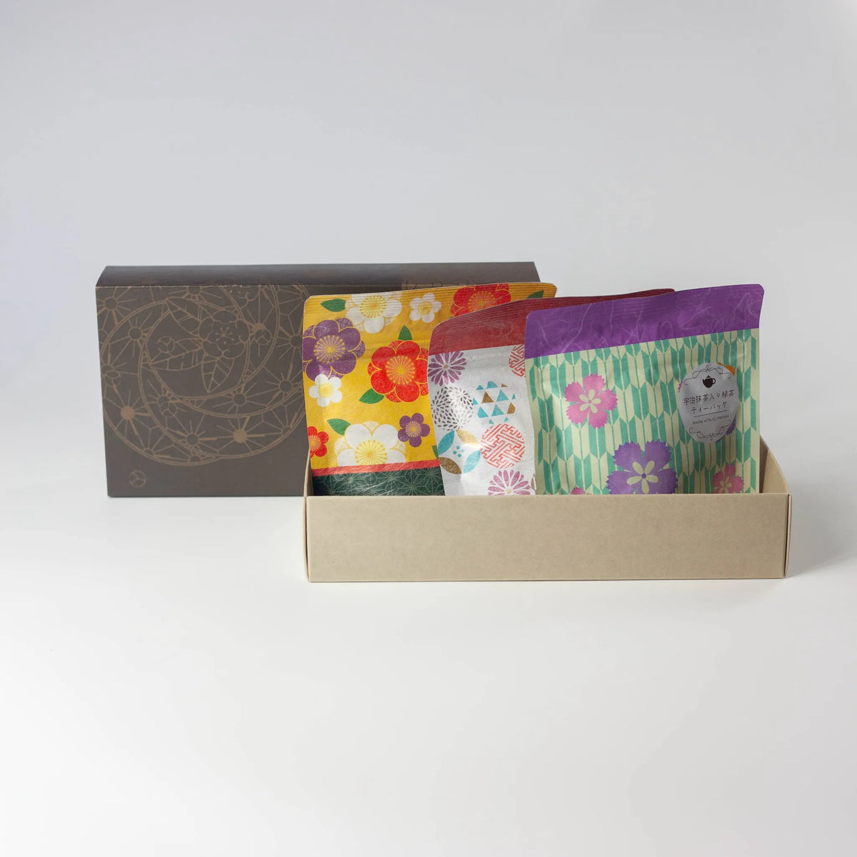 Wafu Japanese Green Tea Gift Set – three colorful floral tea pouches displayed upright in an open gift box tray beside the dark brown lid, on white background
