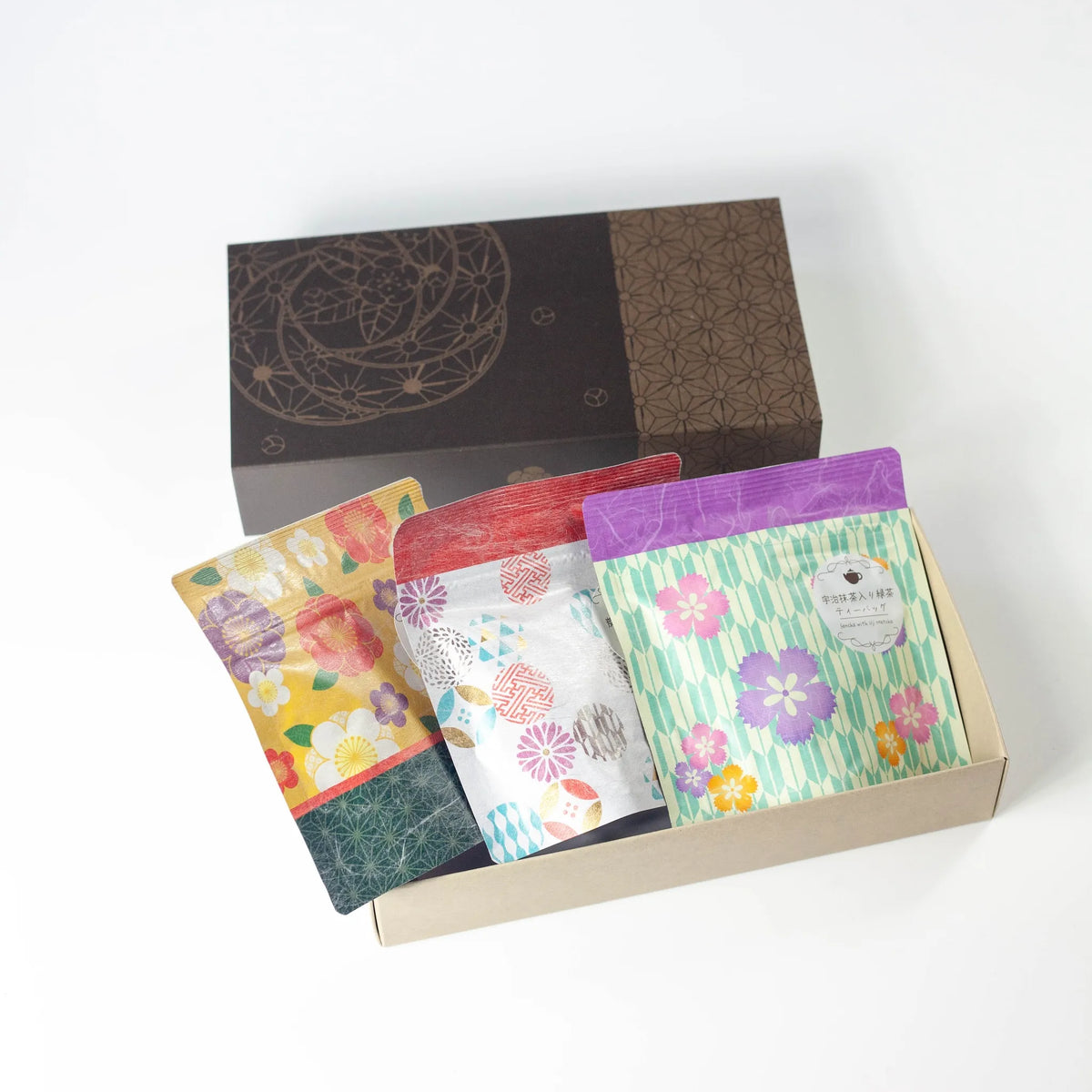 Wafu Japanese Green Tea Gift Set – open dark brown gift box with three colorful floral tea pouches inside: yellow floral sencha, white geometric hojicha, and green floral matcha green tea, on white background
