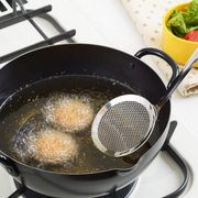 Perforated Oil Skimmer removing oil residue from hot frying oil while korokke (croquettes) fry in black iron tempura pot on gas stove