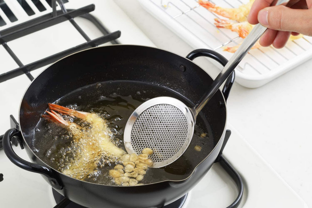 Perforated Oil Skimmer in use skimming oil while shrimp tempura fries in black iron tempura pot on gas stove