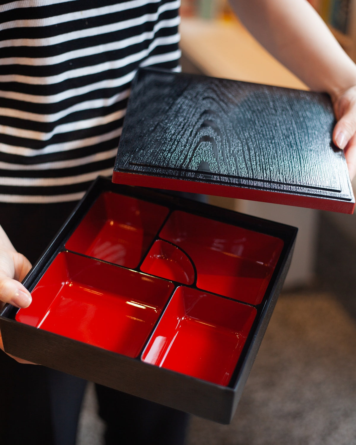 Japanese lacquerware-style bento box with black wood-grain textured lid and dark red base, elegant square lunch box, made in Japan