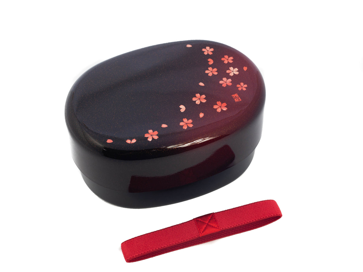 Hakoya Sakura Petals Oval Bento Box closed, black to burgundy lacquer with scattered pink cherry blossom pattern, angled view on grey background