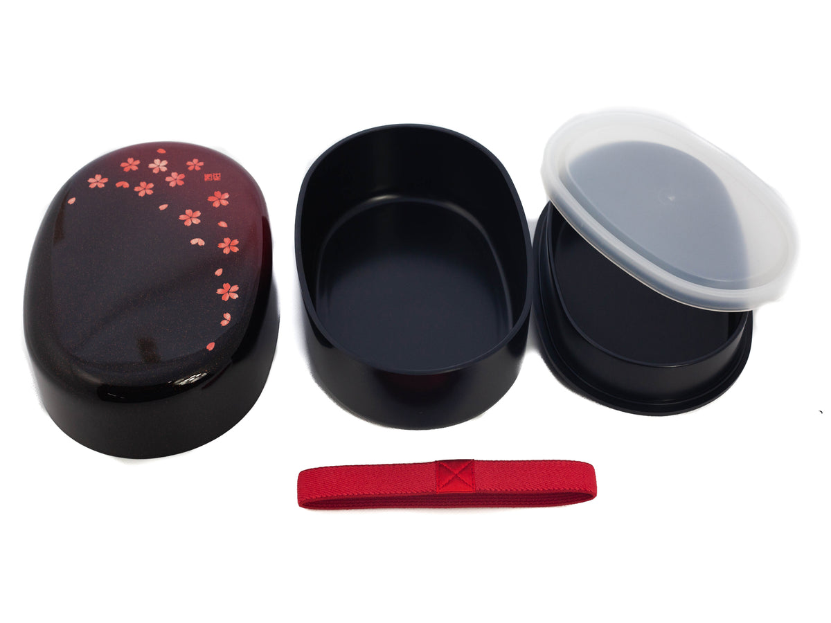 Hakoya Sakura Petals Oval Bento Box closed, black to burgundy lacquer with scattered pink cherry blossom pattern, angled view on grey background
