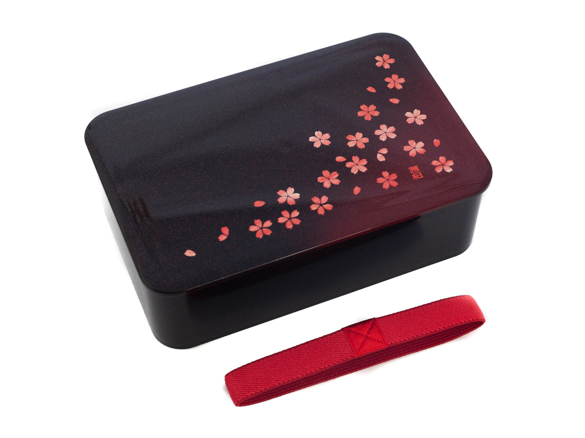 Hakoya Sakura Petals Bento Box closed, black to burgundy gradient lacquer lid with scattered pink cherry blossom pattern, angled view on grey background