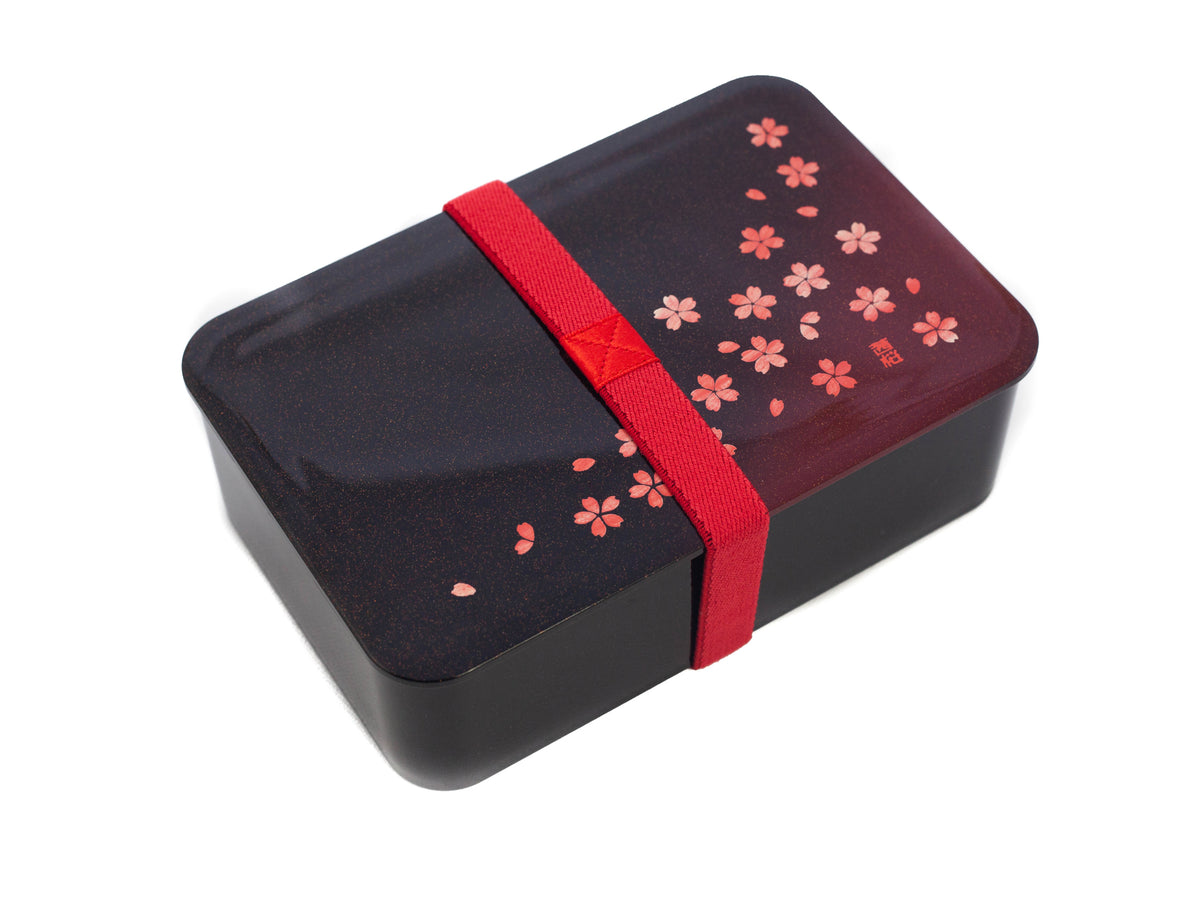 Hakoya Sakura Petals Bento Box closed, black to burgundy gradient lacquer lid with scattered pink cherry blossom pattern, angled view on grey background