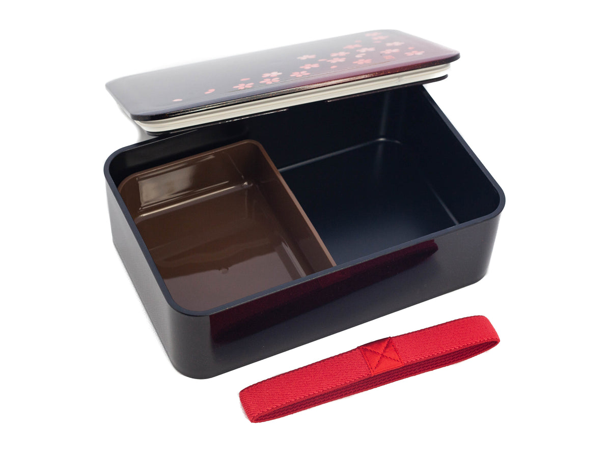 Hakoya Sakura Petals Bento Box closed, black to burgundy gradient lacquer lid with scattered pink cherry blossom pattern, angled view on grey background