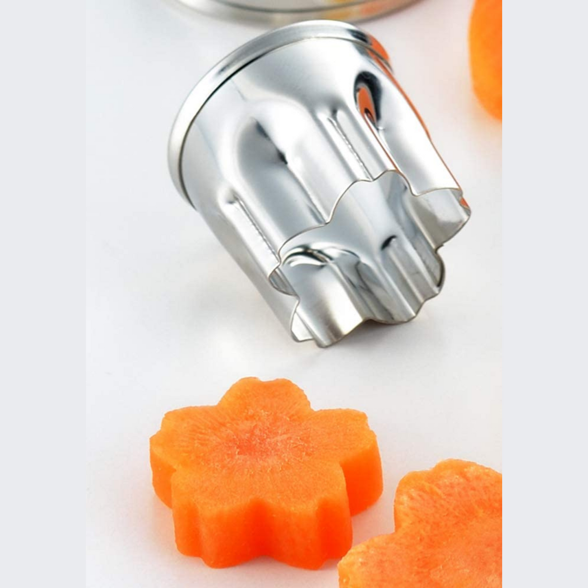Close-up of Sakura Cutter Set small flower cutter pressing into carrot slice, with sakura-shaped carrot pieces beside it
