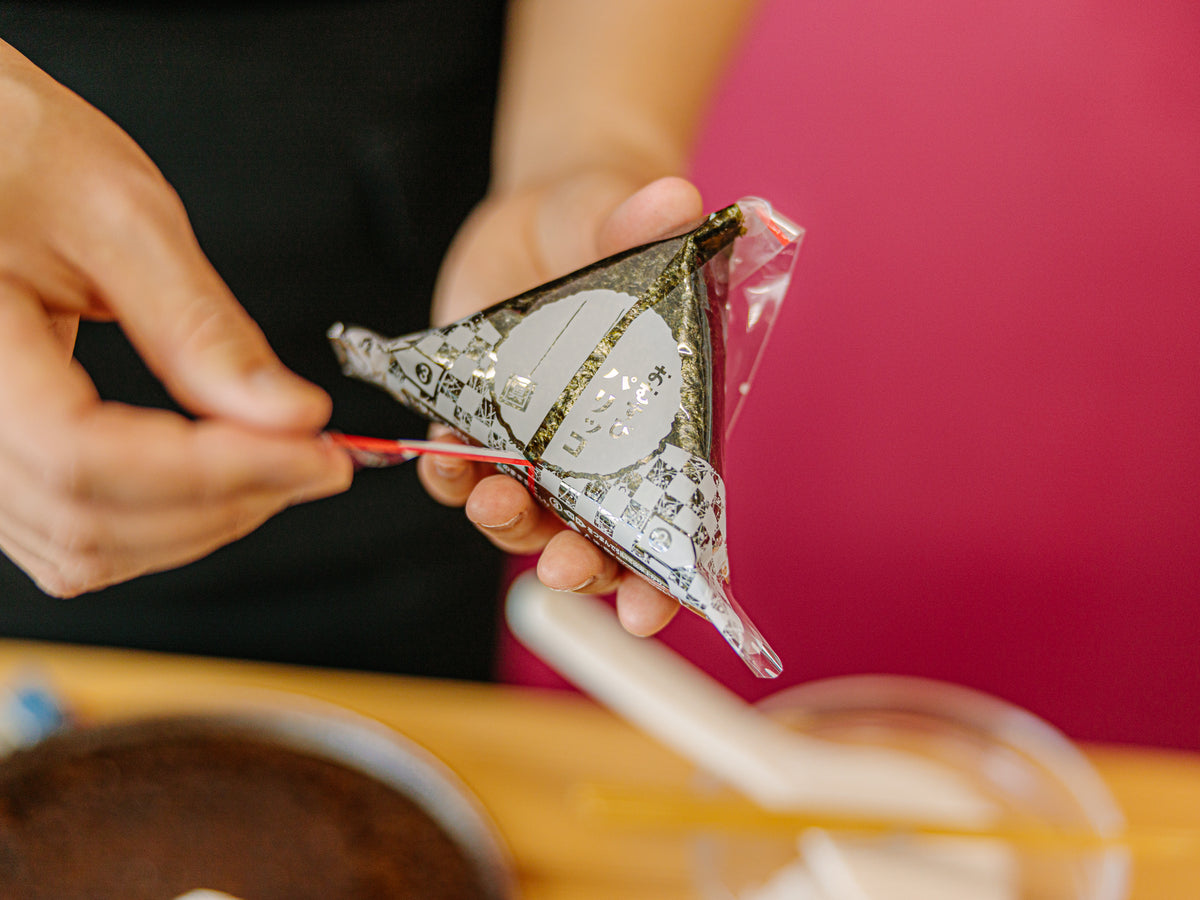 Hands pulling plastic film from Japanese rice ball packaging – Bento&co