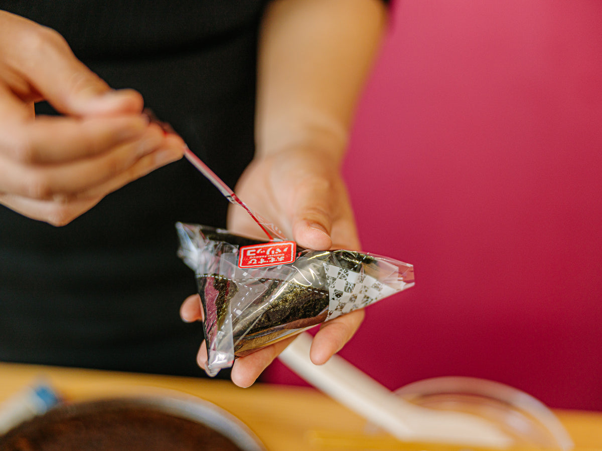 Hands pulling plastic film from Japanese rice ball packaging – Bento&co