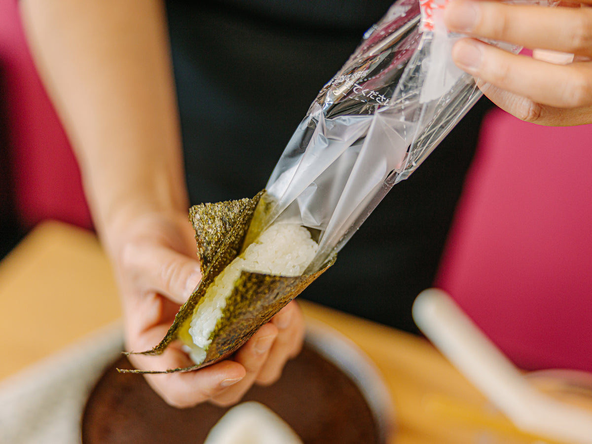 Hands pulling plastic film from Japanese rice ball packaging – Bento&co